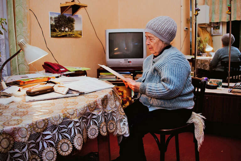 ältere Frau sitzt an einem Tisch und liest eine Zeitschrift