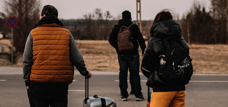 Flüchtlinge stehen mit Koffer am Straßenrand
