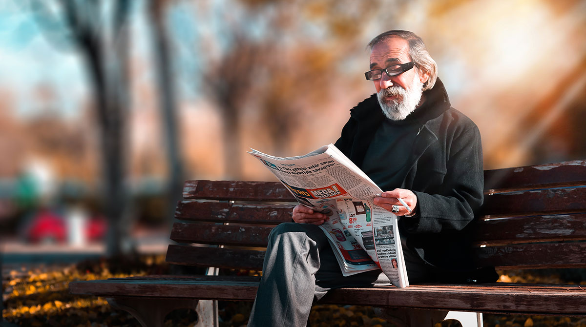 älterer Mann liest Zeitung auf einer Parkbank