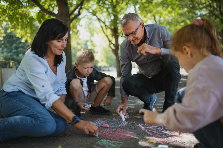 Zwei Erwachsene und zwei Kinder malen mit Kreide auf der Straße