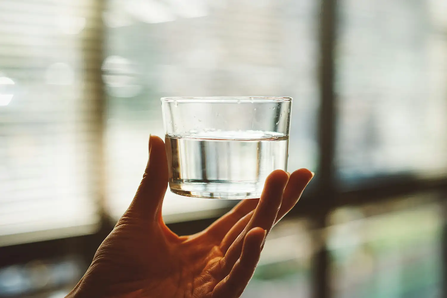Auf dem Bild sieht man eine Hand, die ein halb gefülltes Glas Wasser hält